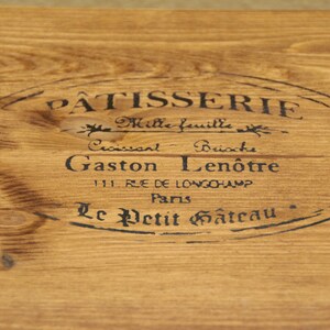 May include: A wooden sign with a black oval stamp that reads "PATISSERIE Mille feuille Croissant Brioche Gaston Len&ocirc;tre 111. RLE DE LONGCHAMP Paris Le Petit G&acirc;teau".