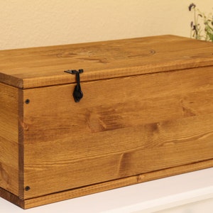 May include: A wooden storage box with a hinged lid and two black metal clasps. The box is stained a dark brown color and has a natural wood grain.