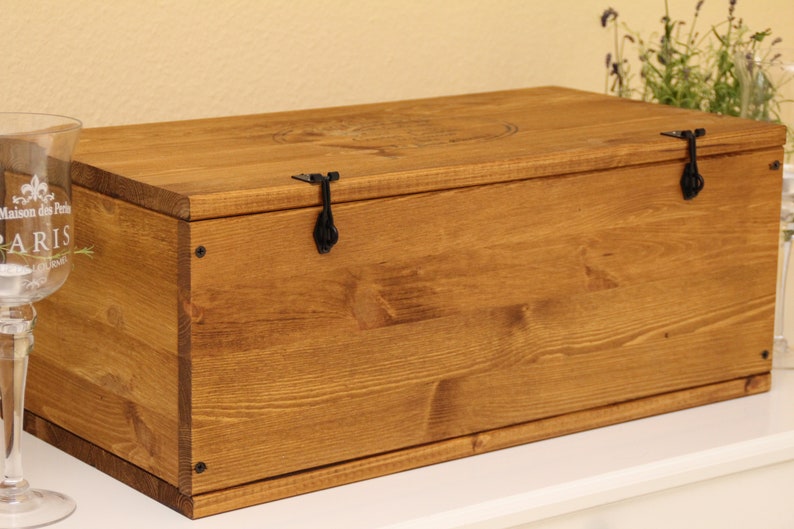 May include: A wooden storage box with a hinged lid and two black metal clasps. The box is stained a dark brown color and has a natural wood grain.