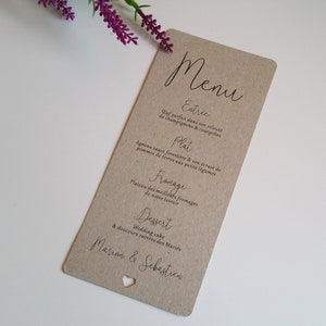 Peut inclure: Une carte de menu en papier kraft avec une découpe en forme de cœur. Le menu est écrit en français et comprend les éléments suivants : Estree, Plat, Franage, Dessert. Le menu est pour un mariage et comprend les noms Marion & Sebastien.