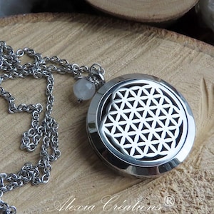 Può includere: Una collana color argento con un ciondolo rotondo con un design geometrico a fiore della vita. La collana è su una superficie di legno, con un disco di legno inciso con fasi lunari e formazioni di cristalli bianchi sullo sfondo.