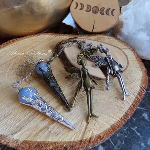 Peut inclure: Trois pendules en argent et bronze sur le thème des fées avec des pointes de cristal bleu. Les pendules sont sur une surface en bois avec un cristal et un motif de phases lunaires en bois en arrière-plan.