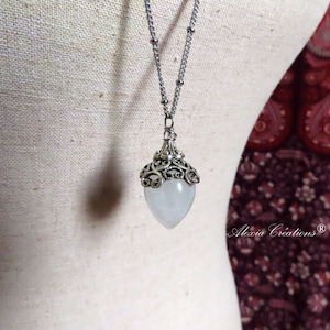 May include: A silver chain necklace with a white, teardrop-shaped pendant. The pendant is surrounded by a silver filigree design.