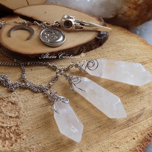 Op de afbeelding: Een zilveren ketting met drie heldere kwartskristal hangers die zijn gewikkeld in zilverdraad. De ketting heeft ook een zilveren halve maan hanger en een zilveren hanger met een stervormig ontwerp.