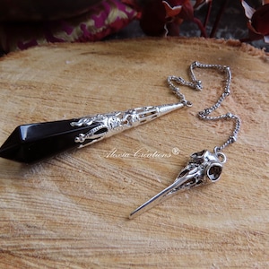 Puede incluir: Pendulo de cristal negro con un diseño plateado adornado y un péndulo en forma de calavera plateado en una cadena plateada.