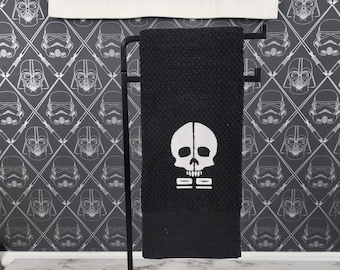 Símbolo inspirado en Clone Force 99 bordado en blanco sobre una toalla de cocina negra.