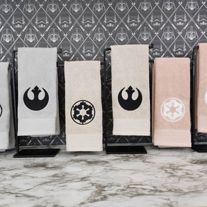 Puede incluir: Conjunto de seis toallas de cocina con bordados de temática de Star Wars. Dos toallas presentan el símbolo de la Alianza Rebelde en blanco y negro, y dos toallas presentan el símbolo imperial en blanco y negro. Las dos toallas restantes presentan el símbolo de la Alianza Rebelde en blanco y el símbolo imperial en blanco.