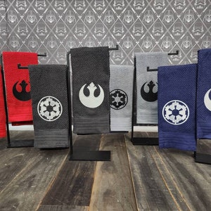 Puede incluir: Conjunto de ocho toallas de cocina con bordados de temática de Star Wars. Las toallas son de varios colores, incluyendo rojo, negro, gris y azul. Cada toalla tiene un diseño diferente, incluyendo el símbolo de la Alianza Rebelde y el símbolo Imperial.
