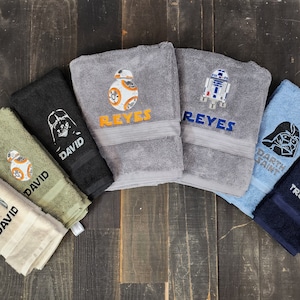 Könnte beinhalten: Ein Set aus sechs Handtüchern mit Star Wars-Charakteren und Namen. Die Handtücher sind in verschiedenen Farben, darunter Schwarz, Grün, Grau, Blau und Weiß. Die Charaktere sind Darth Vader, R2-D2, BB-8 und ein Stormtrooper.