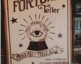 May include: A wooden sign with the text "FORTUNE Teller" and a drawing of a crystal ball with the words "PAST PRESENT FUTURE" and "SEES ALL TELLS ALL". The sign also includes the text "TAROT ASTROLOGY TEA LEAVES CRYSTAL BALL".