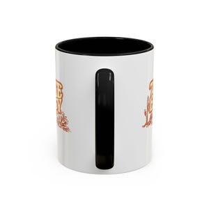 Puede incluir: Taza de cer&aacute;mica blanca con interior y asa negros. La taza presenta el texto "THE BUSY" en marr&oacute;n, con ilustraciones de cactus y follaje. Dise&ntilde;ada para bebidas calientes.