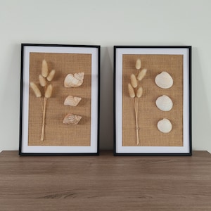 May include: Two black framed pictures with burlap backgrounds. The pictures feature dried pampas grass and seashells.