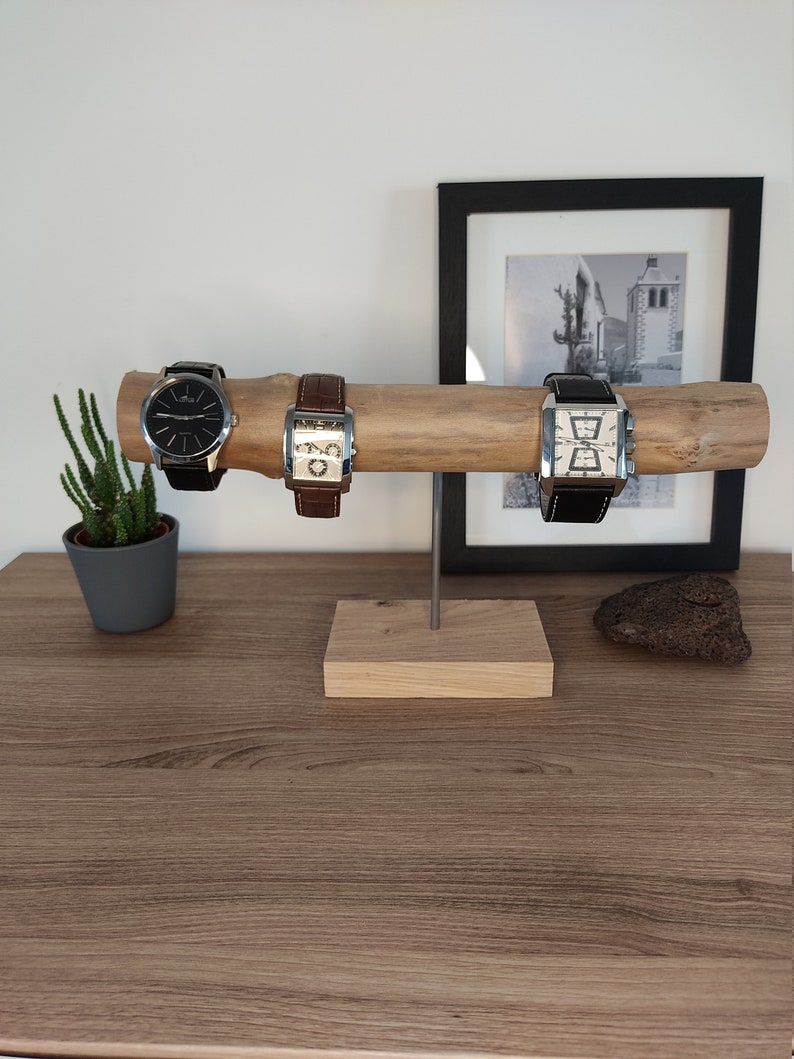 May include: A wooden watch stand with three watches on it. The stand is made of a natural branch with a square wooden base. The watches have brown leather bands and silver cases.
