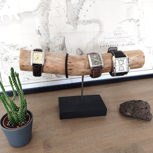 May include: Three wristwatches with brown leather bands are displayed on a wooden stand. The stand is on a black base and is on a wooden surface. The watches have silver cases and white faces.