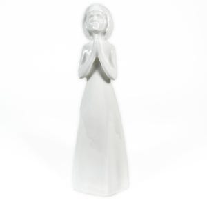 May include: A white ceramic figurine of a girl with her hands clasped in prayer. The figurine has a simple, elegant design with a smooth, glossy finish. The girl is wearing a long dress and has short hair. The figurine is standing upright.
