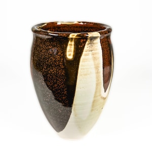 Peut inclure: Un vase en céramique fait à la main avec un design unique. Le vase présente une finition marron foncé mouchetée d'un côté, passant à un blanc crème et marron clair de l'autre. Le bord a un glaçage marron foncé brillant.