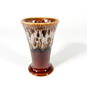 Peut inclure: Un vase en céramique marron avec un dessus évasé et une base en piédestal. Le vase présente un motif moucheté dans des tons de marron et de blanc, avec une finition brillante. Le vase mesure environ 15 cm de haut.