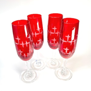 Könnte beinhalten: Ein Set aus vier hohen Champagnergläsern aus leuchtend rotem Glas. Jedes Glas ist mit einem klaren, geätzten Stern- oder Kreuzschraffurmuster um den Kelch versehen. Die Gläser haben schlanke, klare Stiele und runde Füße und stehen aufrecht.