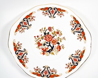 May include: A white oval ceramic cake plate with a gold rim and a floral design in shades of red, orange, blue, and gold.