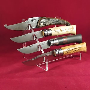 K&ouml;nnte beinhalten: Vier verschiedene Taschenmesser mit Holzgriffen werden auf einem durchsichtigen Acrylst&auml;nder pr&auml;sentiert. Die Messer haben unterschiedlich farbige Griffe, darunter braun, beige, schwarz und olivfarbenes Holz. Die Messer sind alle geschlossen und haben eine silberne Klinge.