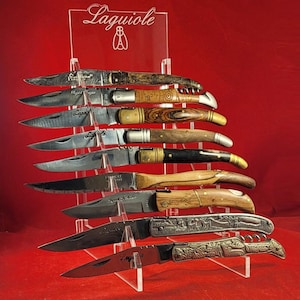 May include: A set of nine Laguiole pocket knives with wooden handles displayed on a clear acrylic stand. The knives have different designs and finishes, including a corkscrew.