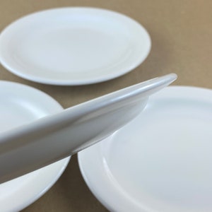 以下が含まれることがあります： 3枚の白いセラミック製のプレートが積み重ねられています。 上のプレートが少し傾いており、下のプレートの縁が見えています。