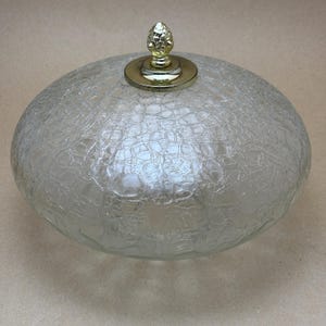 Pode incluir: Uma luminária de vidro transparente texturizado com um pináculo e base dourados. A luminária tem formato oval e um padrão rachado, adequado para montagem no teto ou na parede. O pináculo é um elemento decorativo.