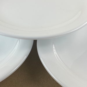 以下が含まれることがあります： 3枚の白いセラミック製のプレートが積み重ねられています。プレートはシンプルで、わずかに盛り上がった縁があります。