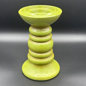May include: A lime green candle holder with a stacked, rounded design. The base and top are wider than the central column, which is composed of several stacked, rounded sections. The candle holder has a glossy finish and is set against a black background.