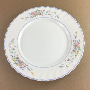Puede incluir: Plato de cerámica blanco con borde festoneado y ribete azul. El plato está decorado con un estampado floral en colores pastel, incluyendo rosa, azul y amarillo. Un diseño delicado y elegante para servir comidas.