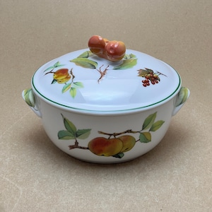 Puede incluir: Plato de porcelana blanca para hornear con tapa. El plato tiene un borde verde y un diseño floral con manzanas, hojas y bayas. La tapa tiene un pomo en forma de dos manzanas.