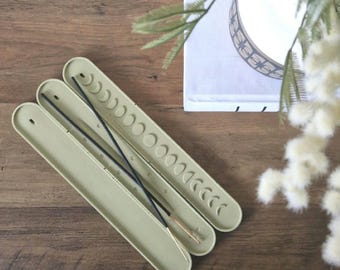 May include: A set of three sage green incense holders with moon phases etched into the surface. The holders are stacked on top of each other and have three incense sticks inside.