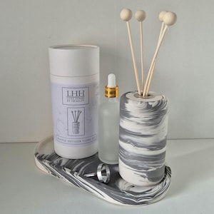 Peut inclure: Un ensemble diffuseur à motif marbré comprenant un récipient cylindrique avec des bâtonnets en bois, une bouteille en verre avec un compte-gouttes et un plateau assorti. Un récipient cylindrique avec le texte "LHH Luxe Homes by Headley" est également inclus.