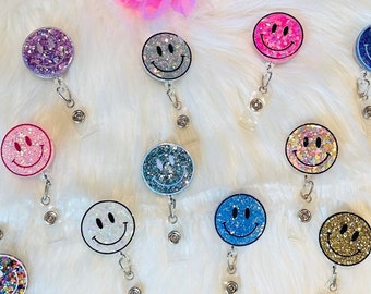 Puede incluir: Surtido de 15 portagajes retráctiles con caritas sonrientes brillantes. Los portagajes son de varios colores, incluyendo rosa, azul, verde, dorado y morado.