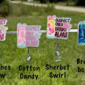 Pu&ograve; includere: Quattro porta badge con accenti glitterati, ognuno con un design a lattina e la scritta "SUSPECT ONLY DRINKS ALANI". I porta badge sono etichettati "Witches Brew", "Cotton Candy", "Sherbet Swirl" e "Breeze Berry".