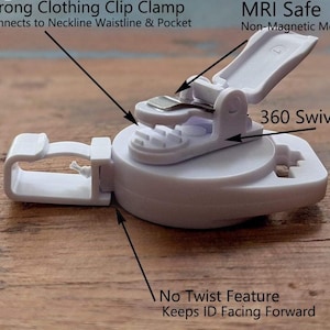 May include: A white plastic clothing clip clamp with a 360-degree swivel. The clip is designed to connect to necklines, waistlines, and pockets. The text on the clip reads "Strong Clothing Clip Clamp" and "MRI Safe."