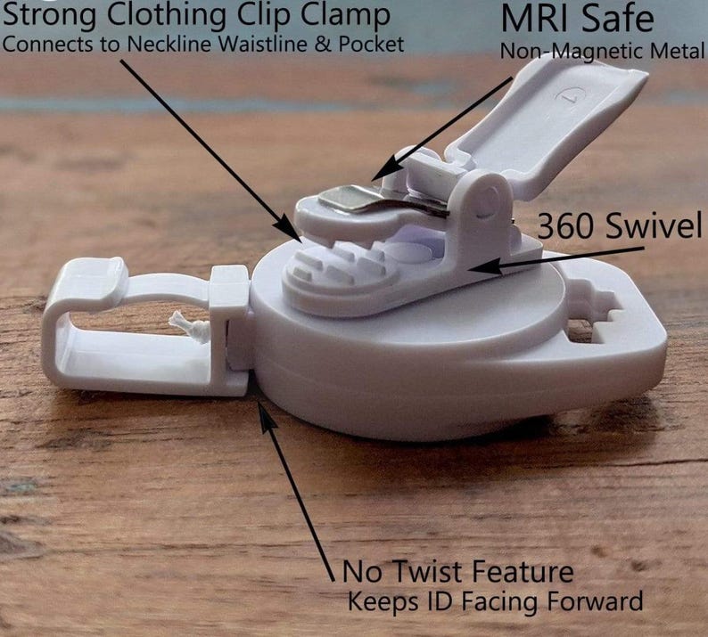 May include: A white plastic clothing clip clamp with a 360-degree swivel. The clip is designed to connect to necklines, waistlines, and pockets. The text on the clip reads "Strong Clothing Clip Clamp" and "MRI Safe."