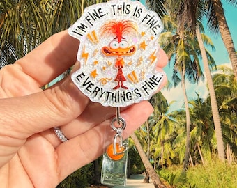 May include: A clear acrylic badge reel featuring a glittery finish and a cartoon character with wild orange hair and a wide-eyed expression. The text reads I'M FINE. THIS IS FINE. EVERYTHING'S FINE. It includes a silver metal clip and a heart charm.