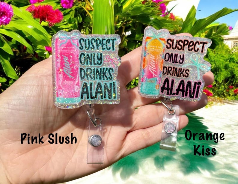 Pu&ograve; includere: Due porta badge con la scritta "SUSPECT ONLY DRINKS ALANI". Uno presenta un design di lattina rosa con l'etichetta "Pink Slush", l'altro ha un design di lattina arancione con l'etichetta "Orange Kiss". Entrambi sono tenuti in mano.