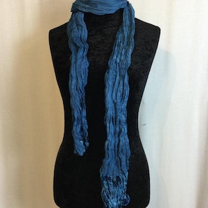 Könnte beinhalten: Ein blauer, geknitterter Schal mit Samtstruktur. Der Schal ist über eine schwarze Schaufensterpuppe gelegt.