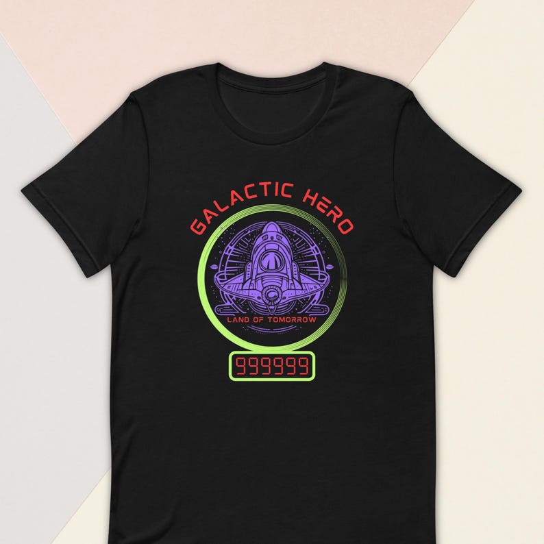 K&ouml;nnte beinhalten: Schwarzes T-Shirt mit einem Grafikdesign, das ein lila Raumschiff in einem gr&uuml;nen und lila Kreis zeigt. Der Text "GALACTIC HERO" ist rot und "LAND OF TOMORROW" gr&uuml;n. Eine Digitalanzeige zeigt "999999".