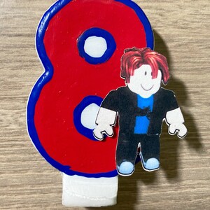 Puede incluir: Vela de cumplea&ntilde;os n&uacute;mero ocho roja y azul con un personaje de Roblox de pie frente a ella. El personaje tiene el pelo rojo, una camisa negra, pantalones azules y una cara blanca.