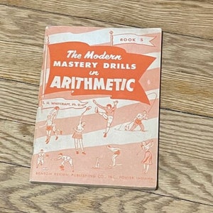May include: A vintage book titled "The Modern Mastery Drills in Arithmetic" with a red, white, and blue cover. The book is illustrated with children playing sports, including baseball, tennis, skiing, and golf.