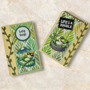 May include: Two greeting cards with frog illustrations. One card features a frog relaxing under an umbrella with the text "Lazy Days." The other card shows a frog in a tire swing with the text "Life's a Jungle."