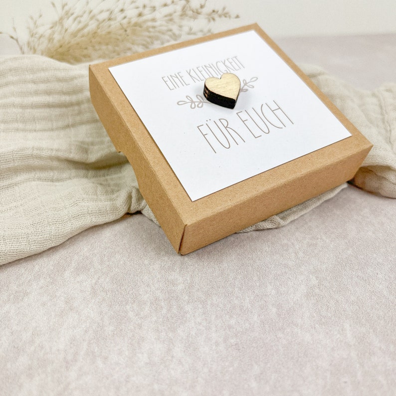 May include: A small brown box with a white card that says "Eine Kleinigkeit f&uuml;r Euch" and a small wooden heart.