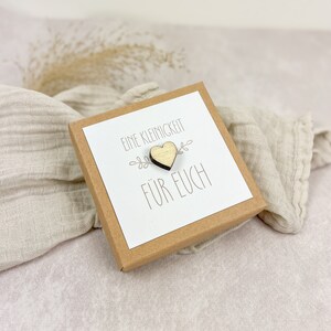 May include: A small brown box with a white card inside. The card has the text "Eine Kleinigkeit f&uuml;r Euch" and a small wooden heart.