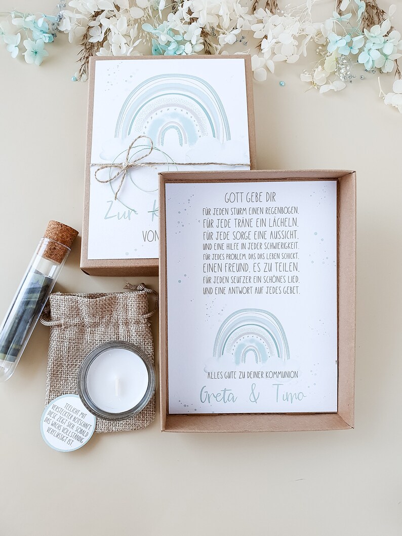 May include: A gift box with a card that reads "Gott gebe dir" and a rainbow design. The card includes a message about finding strength and support in life. The box also contains a small candle and a glass tube with a small piece of paper inside.