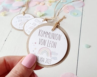 May include: Circular gift tags with the text "KOMMUNION VON LEON" and the date "20. MAI 2023". Each tag features a rainbow and cloud design. The tags are made of brown cardstock and have twine attached.
