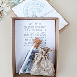 May include: A small brown burlap bag with a drawstring closure, a glass test tube filled with colorful paper scraps, and a card with the text "Gott gebe dir" and a poem in German. The card has a watercolor background with a rainbow design.