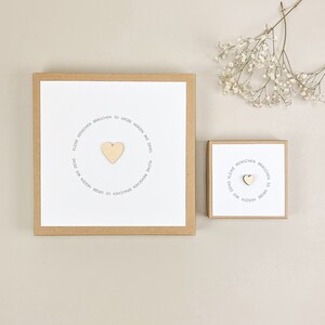 May include: Two brown boxes with white card inserts. The boxes have a circle of text that reads "Kleine Menschen brauchen so gro&szlig;e Herzen wie Deins."  The text is in gray.  A wooden heart is in the center of the circle.